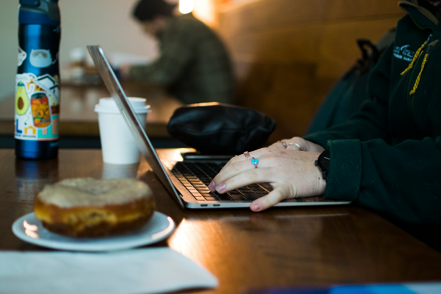 Hände tippen auf einem Laptop an einem Cafétisch mit Kaffee und einem Donut.